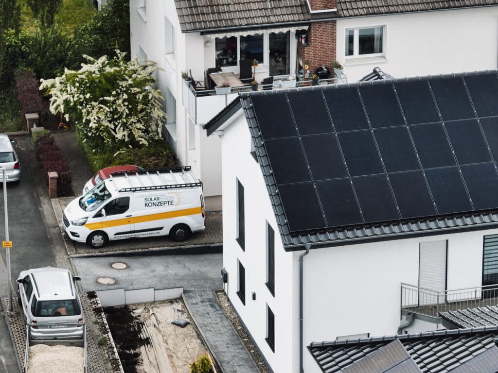 Einsatzfahrzeug von Solarstrom Konzepte parkt neben einem Einfamilienhaus mit frisch installierter Photovoltaikanlage auf dem Ziegeldach – hochwertige Solarmodule für nachhaltige Energiegewinnung im Wohngebiet