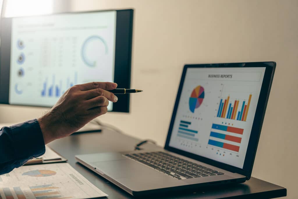 Hand zeigt mit Stift auf Diagramme auf einem Laptop – Auswertung von Geschäftsdaten und Energiekennzahlen.
