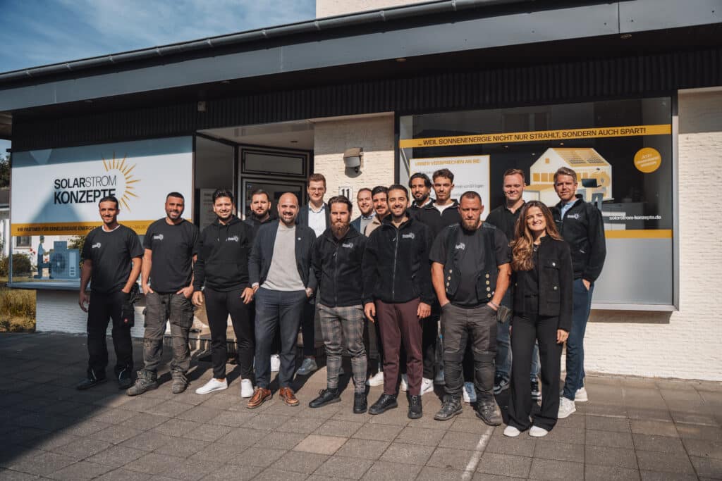 Team von Solarstrom Konzepte mit den Buchstaben Team und stilisierter gelber Sonne im Hintergrund – Symbol für erneuerbare Energien und solare Zukunft, vor der Firma, wir freuen uns